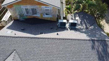 Aerial view of a house roof with a tarp-covered dormer and roof repairs in progress